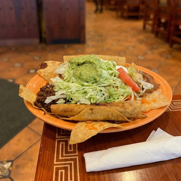 A vibrant orange plate filled with Mexican food, including tacos, nachos, guacamole, and shredded lettuce.