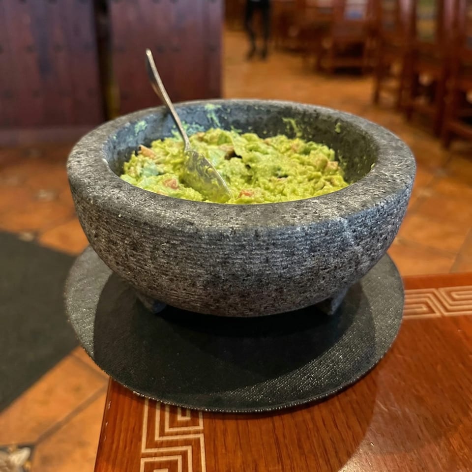 Fresh guacamole in a stone molcajete with a spoon, on a wooden table.