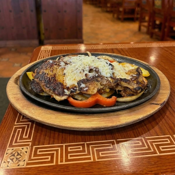 Sizzling fajitas with grilled chicken, melted cheese, bell peppers, and onions on a wooden table.
