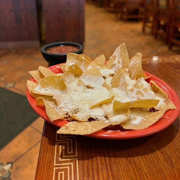 A red plate of cheesy nachos and a side of salsa on a wooden table in a restaurant.