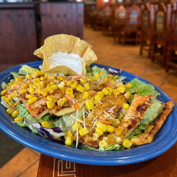 Grilled chicken salad with corn, shredded cheese, and a tortilla bowl of sour cream.