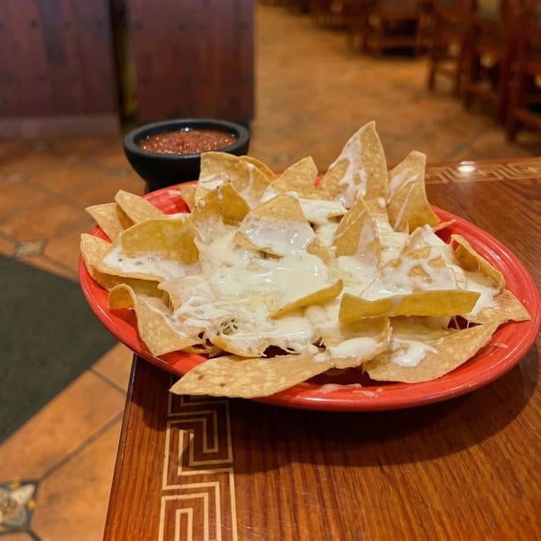 A red plate of nachos covered in white cheese sauce, with a side of salsa.