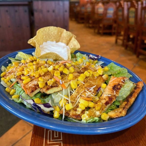 Grilled chicken salad with corn, cheese, and a tortilla bowl of sour cream on a blue plate.