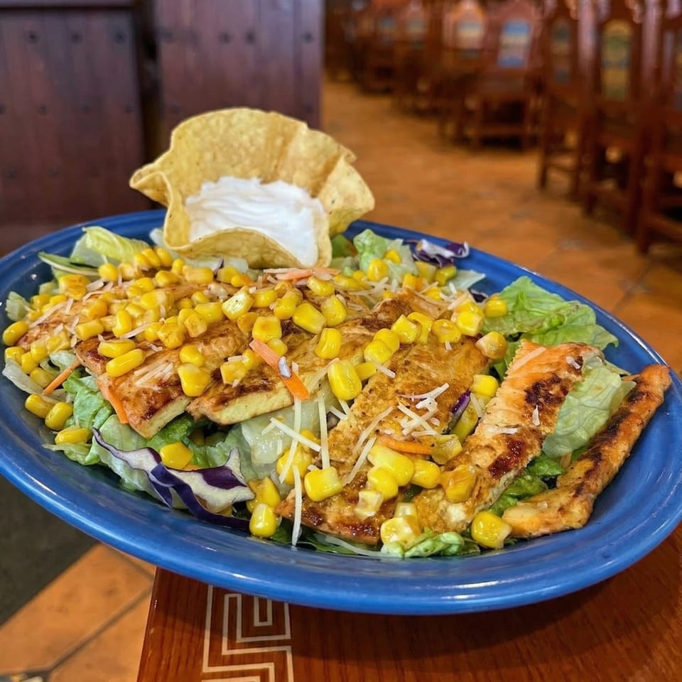 Grilled chicken salad with corn, shredded cheese, and a tortilla bowl of sour cream.