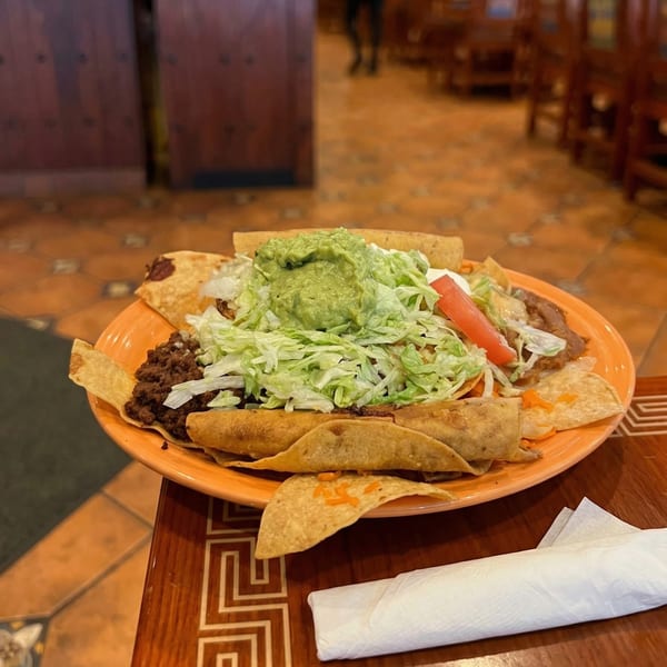 A plate of Mexican food with tacos, nachos, guacamole, lettuce, tomato, and ground beef.