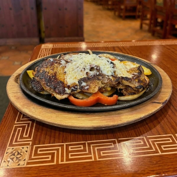 Sizzling fajitas with grilled chicken, melted cheese, onions, and bell peppers on a wooden table.