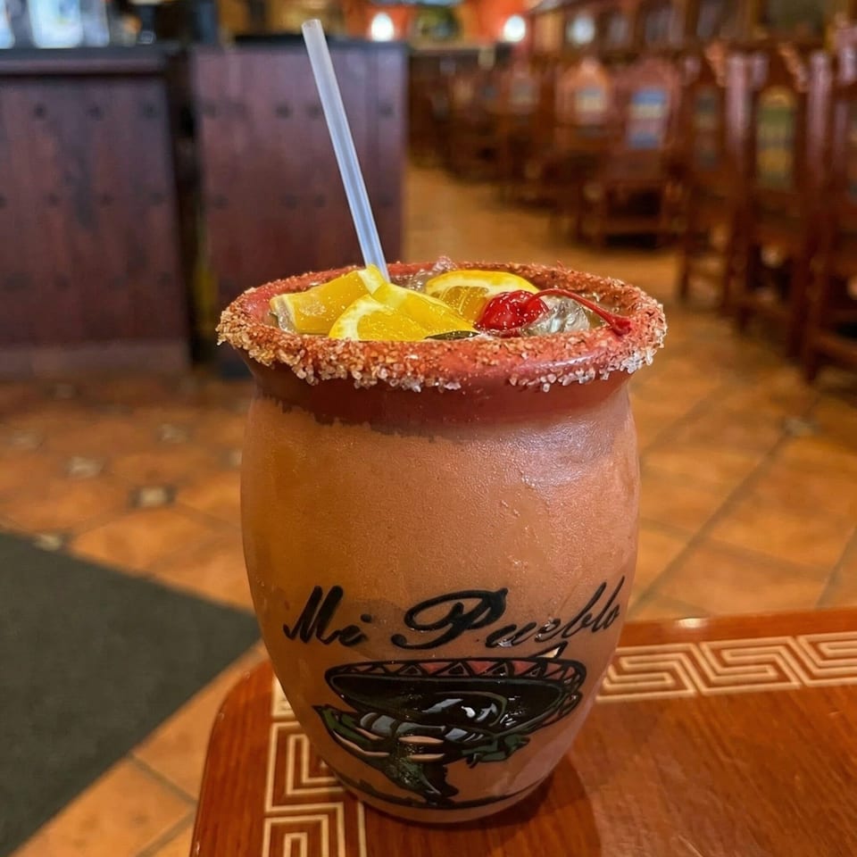 A Mi Pueblo restaurant drink in a clay jar with a salted rim, oranges, and a cherry.