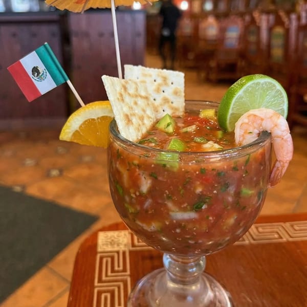 Shrimp cocktail in a goblet, garnished with lime, orange, crackers, and a Mexican flag.