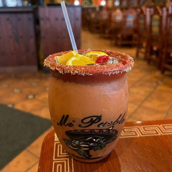 A "Mi Pueblo" branded clay mug with a drink, garnished with orange slices and a cherry.