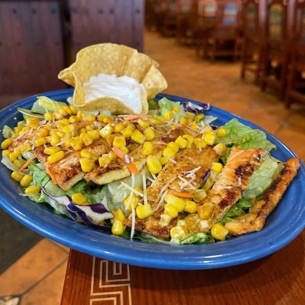 Grilled chicken salad with corn, shredded cheese, and a tortilla chip with sour cream.